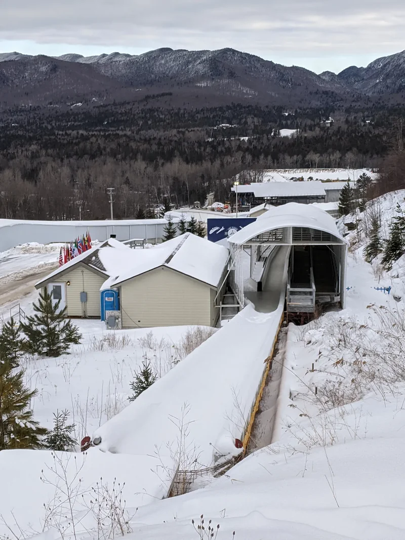 The snowy finish of the Mt Van Hoevenberg bobsled run, with the finish house and the High Peaks behind
