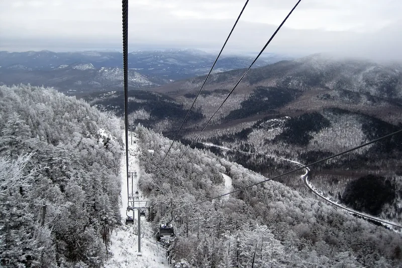 View down the gondola cables from Little Whiteface over frosted evergreen forest and a winding road in the valley