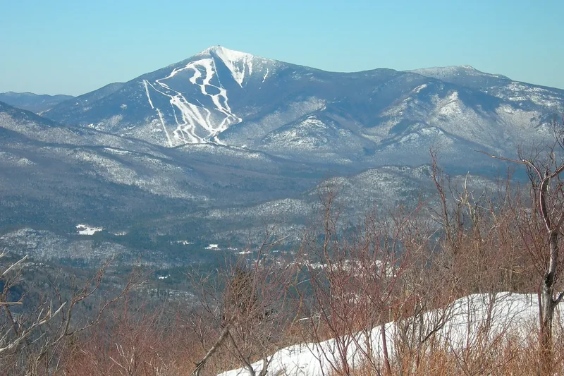 Snow-streaked Whiteface Mountain and Esther Mountain seen across a wooded valley under a clear sky