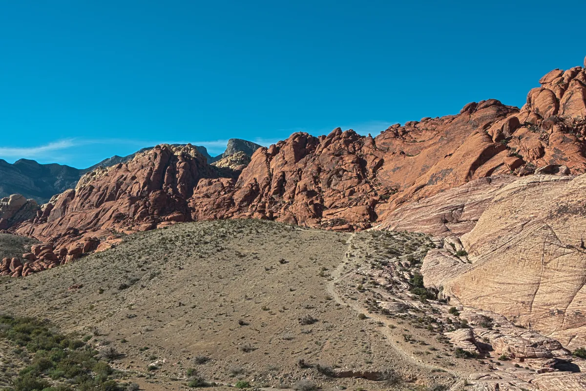 Red sandstone cliffs above a desert trail and scrub at Red Rock Canyon on a clear day