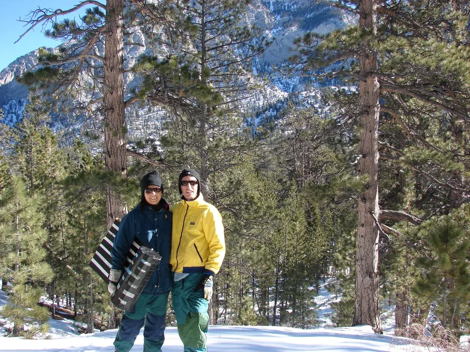 Two people with a sled in deep snow among tall pines in the Spring Mountains