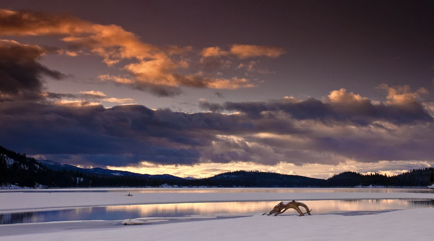 Payette Lake at sunrise with pink light on the water and snowy ridges behind