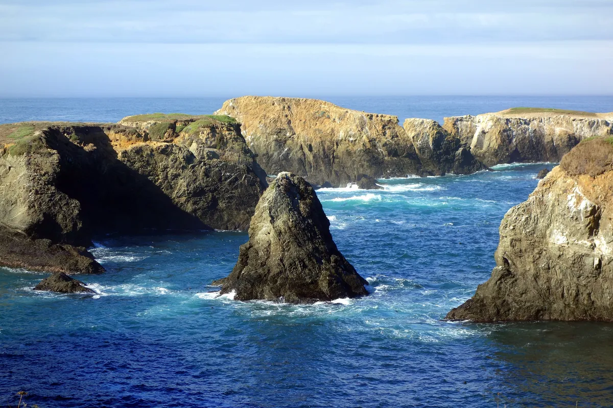 Sea stacks and a rock arch in the surf below the grassy bluffs of Mendocino Headlands State Park
