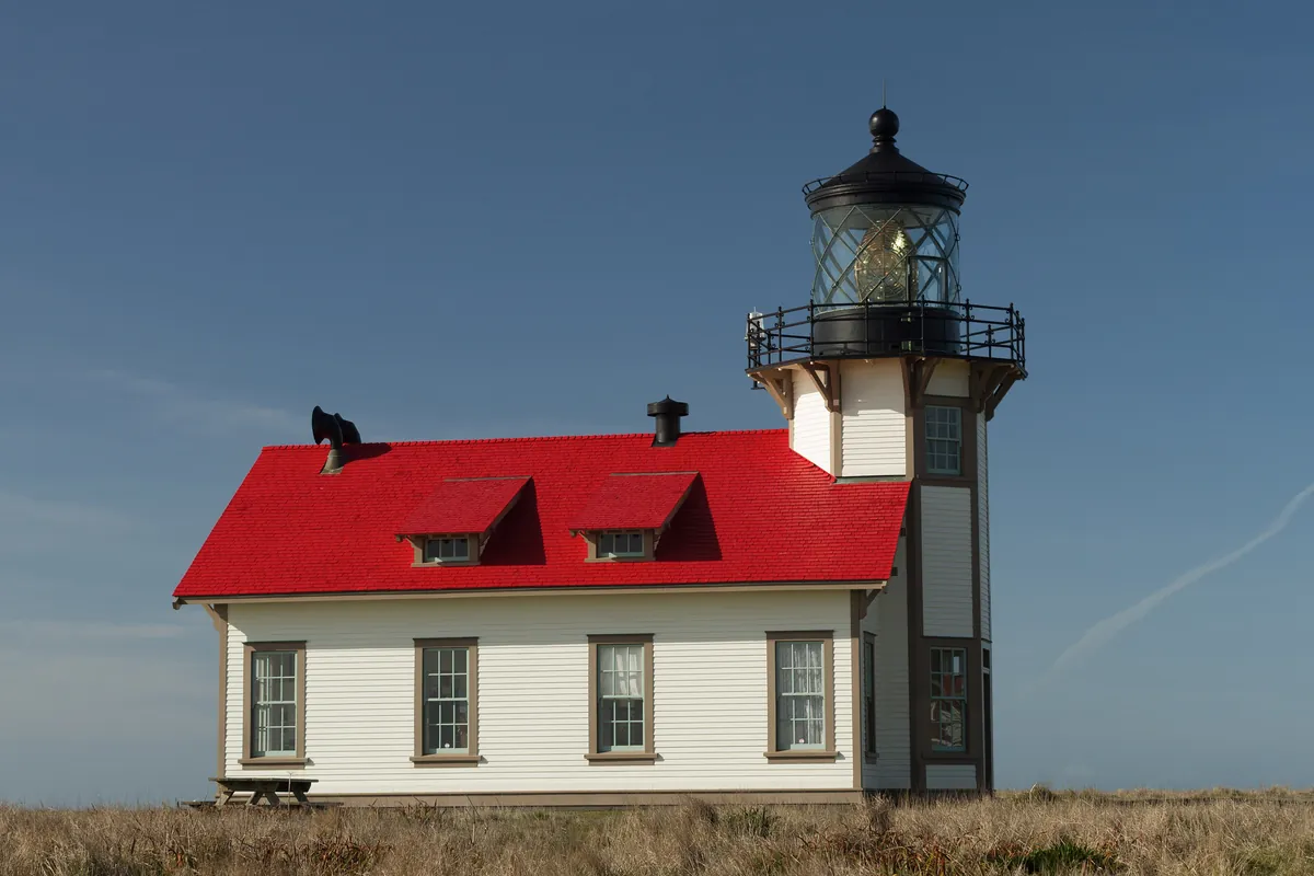The white Point Cabrillo lighthouse with a red roof on an open grassy headland under a blue sky