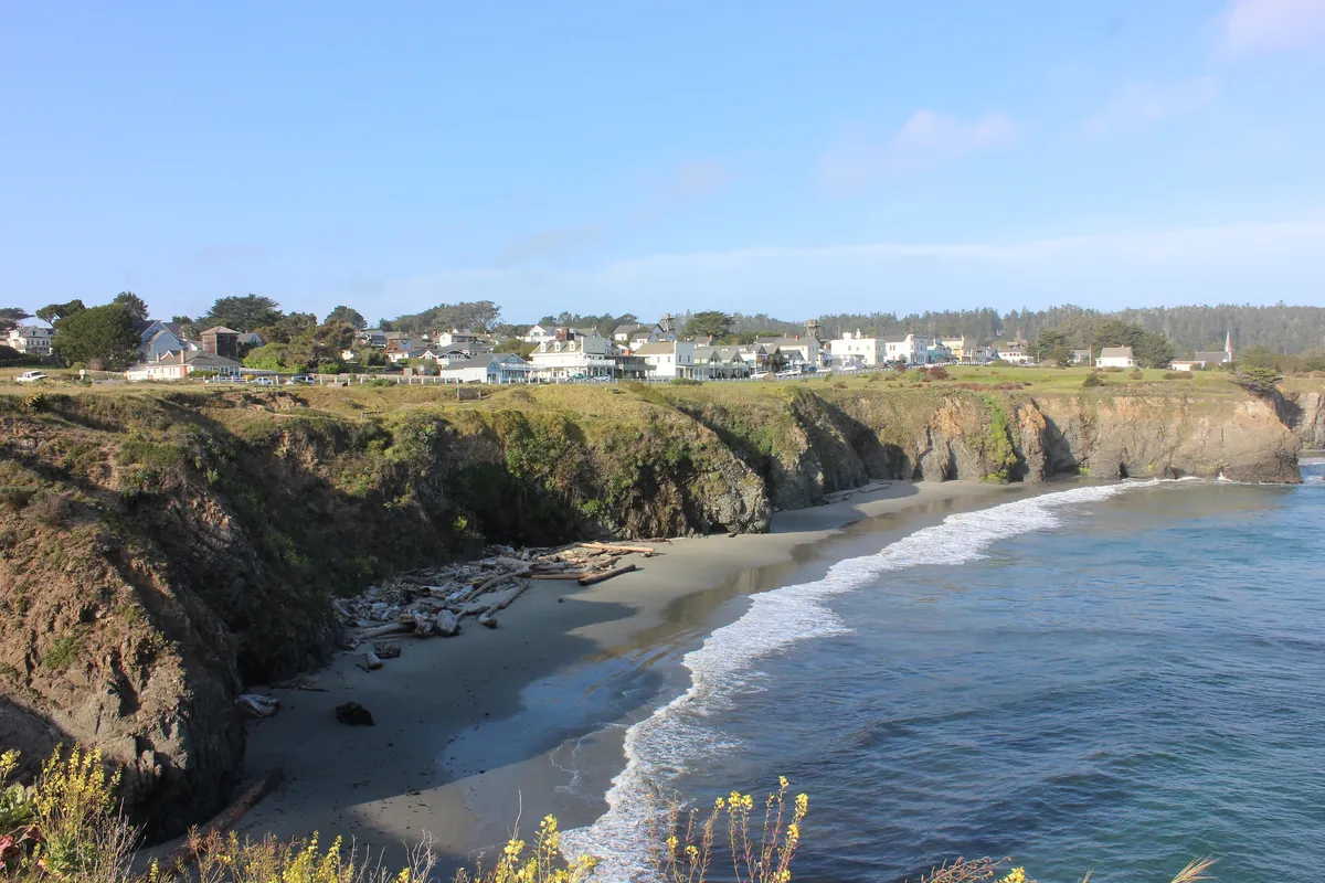 Mendocino village on its bluff above a small beach cove, white wooden buildings and a church spire over the Pacific