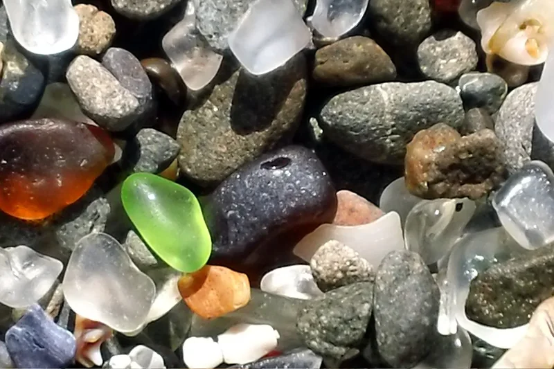 Close-up of smooth sea glass pebbles in green, brown and white mixed with stones at Glass Beach, Fort Bragg