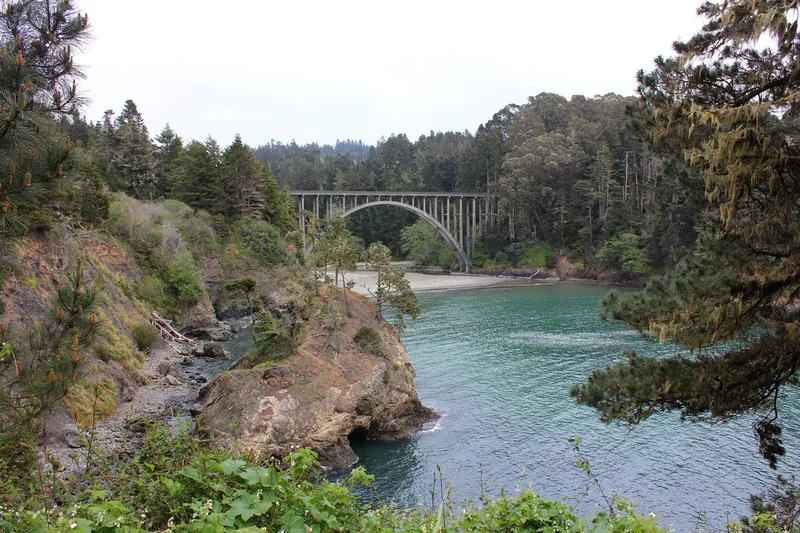 An arched concrete highway bridge over a turquoise cove at Russian Gulch State Park