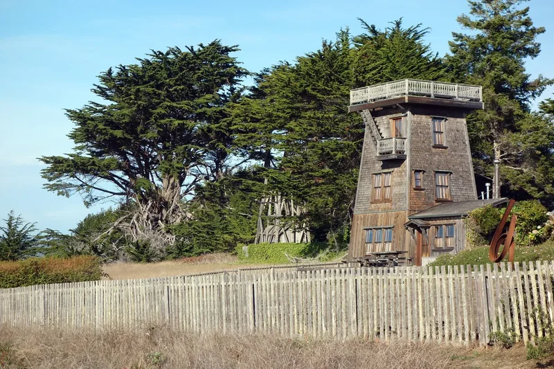 A tall old wooden water tower behind a wooden fence in Mendocino village