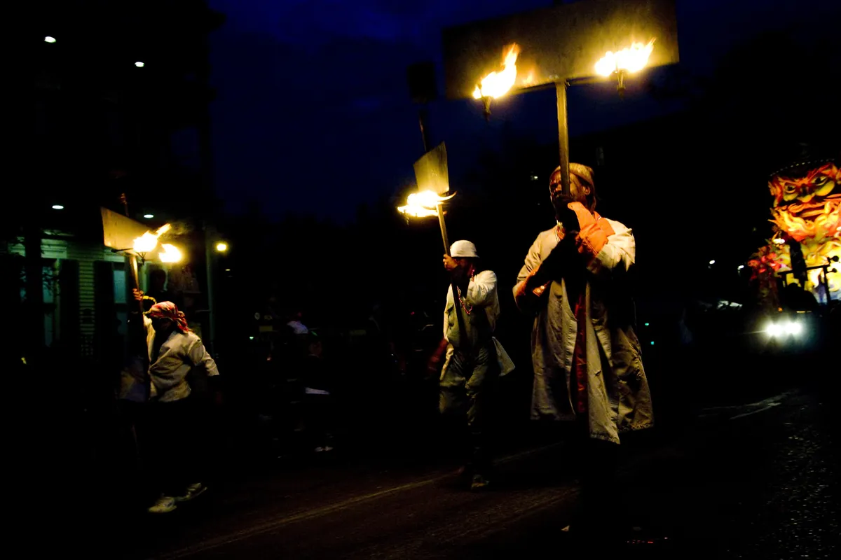 Flambeaux carriers with torches beside a Proteus float at night in New Orleans