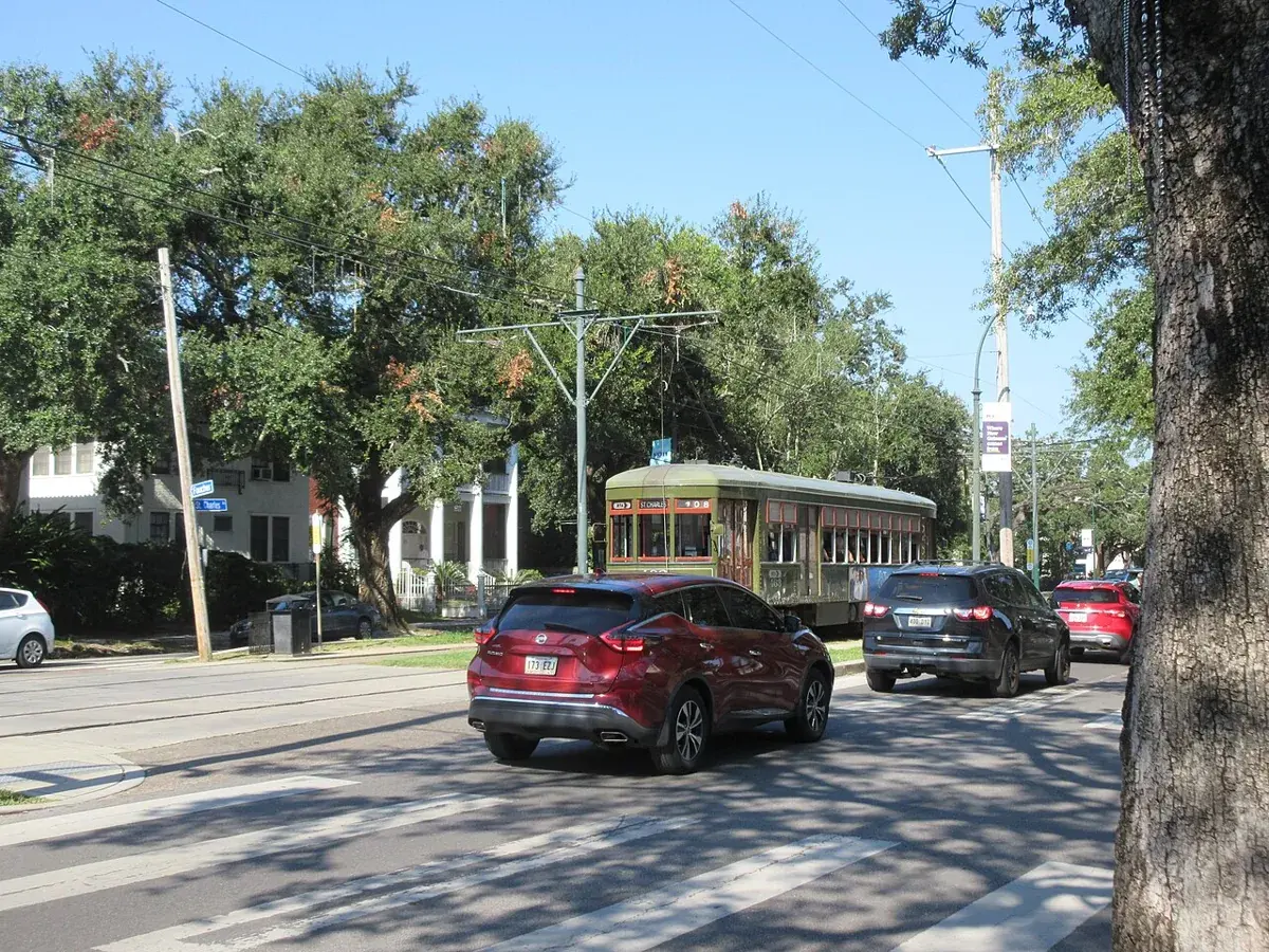 An olive-green St. Charles streetcar running down the median of St. Charles Avenue under live oaks