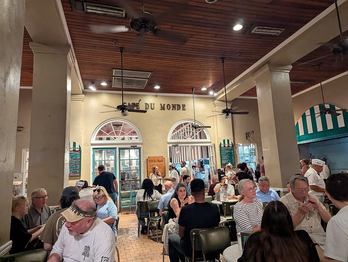 The covered patio of Café du Monde at the French Market, full of people at tables under ceiling fans