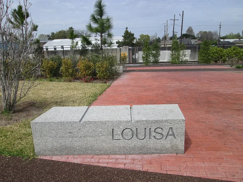 A brick path and a stone marker reading Louisa in Crescent Park in the Bywater