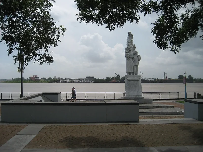 Woldenberg Park on the Mississippi riverfront, a statue and railings by the wide brown river under clouds