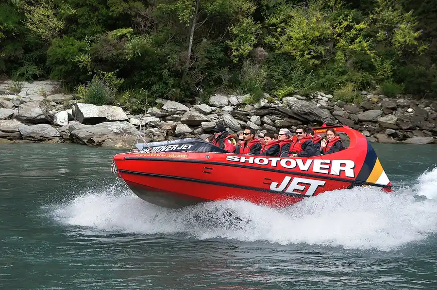 A red Shotover Jet boat racing through the river canyon