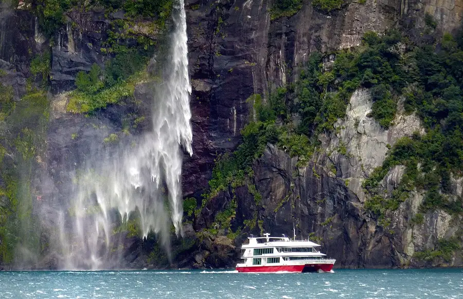 A cruise boat beneath a waterfall in Milford Sound