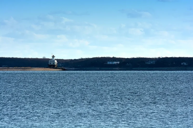 A small lighthouse on a low bar far across calm blue water off the North Fork