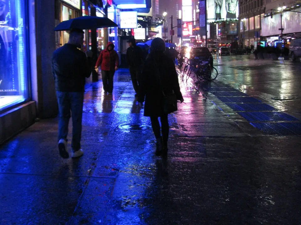 Times Square in the rain at night, with umbrellas and lit billboards reflected on the wet street
