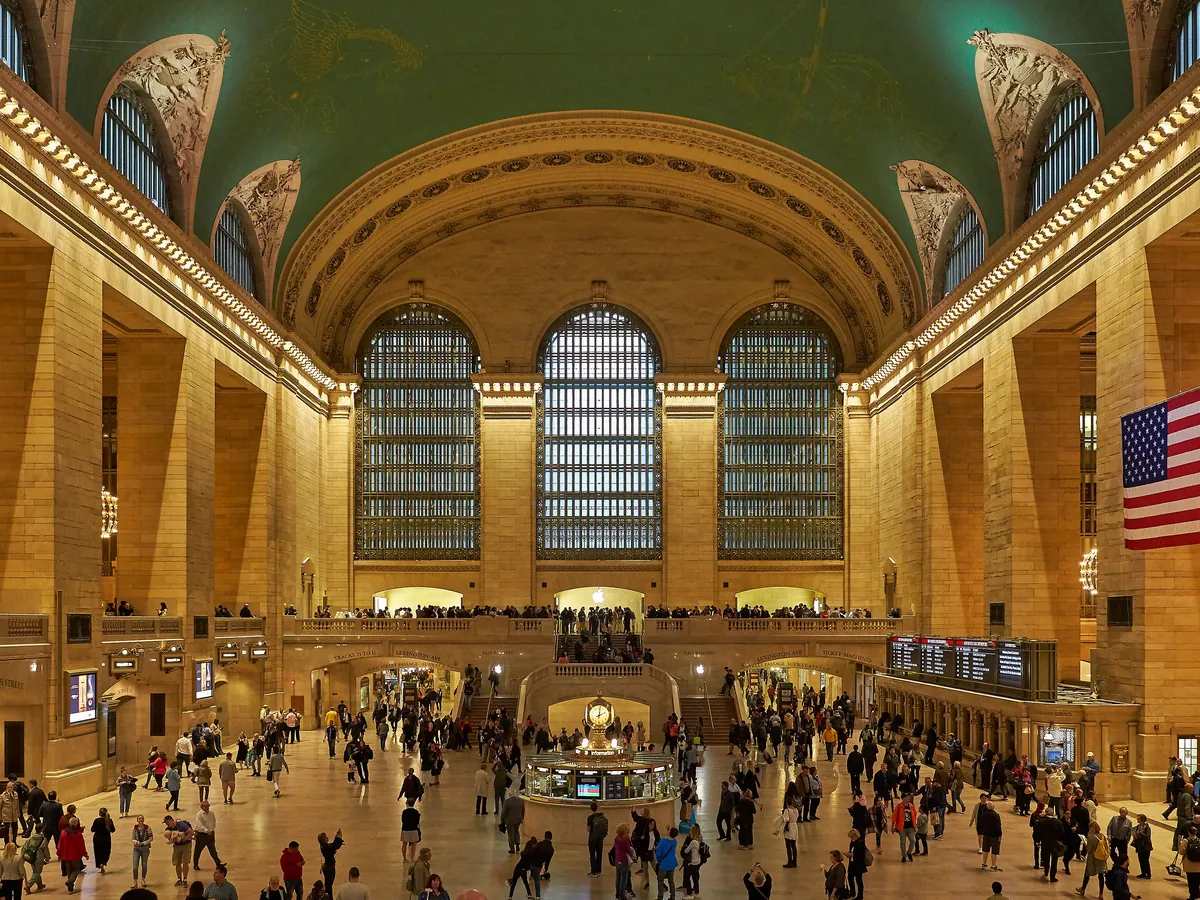 The Main Concourse of Grand Central Terminal at night, with the vaulted ceiling, tall arched windows and the information booth in the middle of the hall
