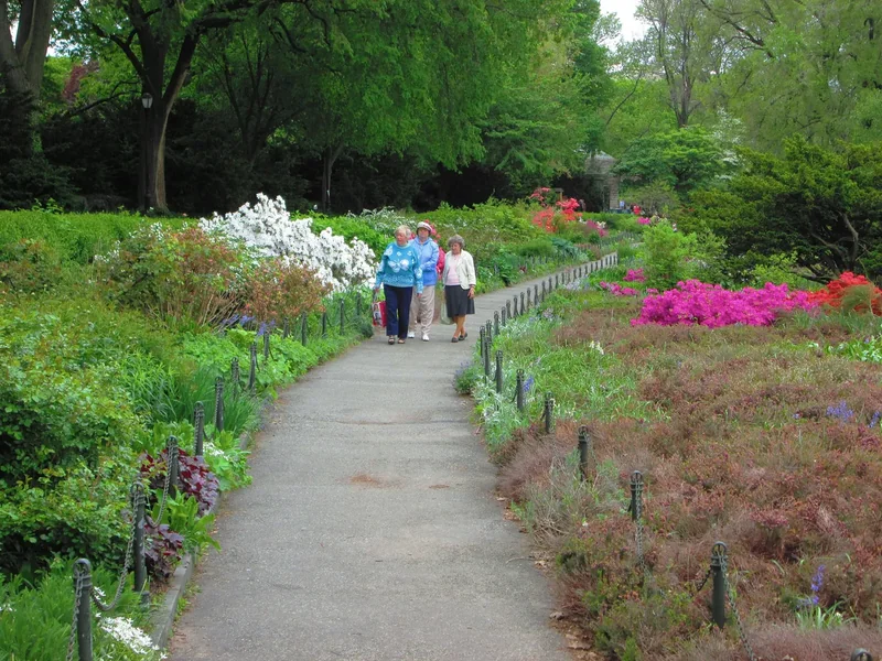 Terraced beds of the Heather Garden in Fort Tryon Park beside a stone wall, with trees and the Hudson beyond
