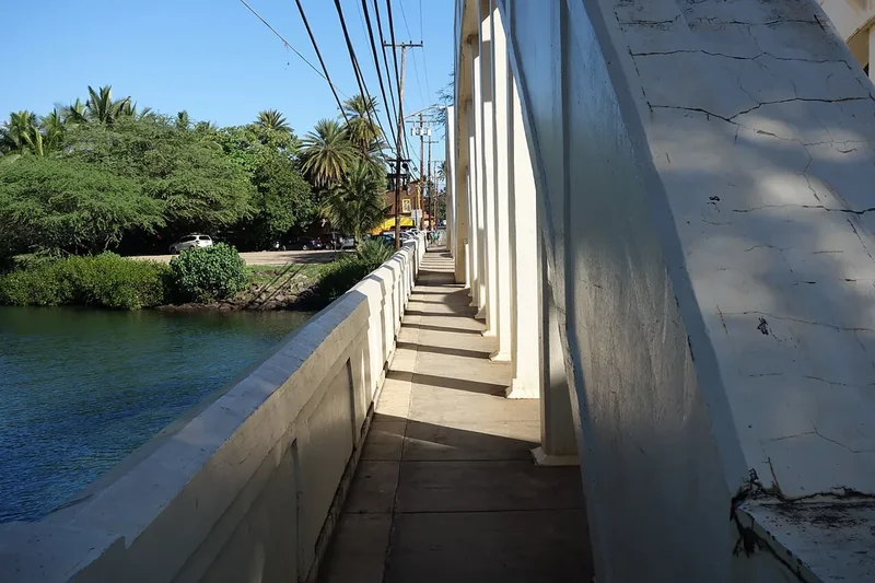 The walkway of the old Anahulu bridge in Haleʻiwa beside the river and palms