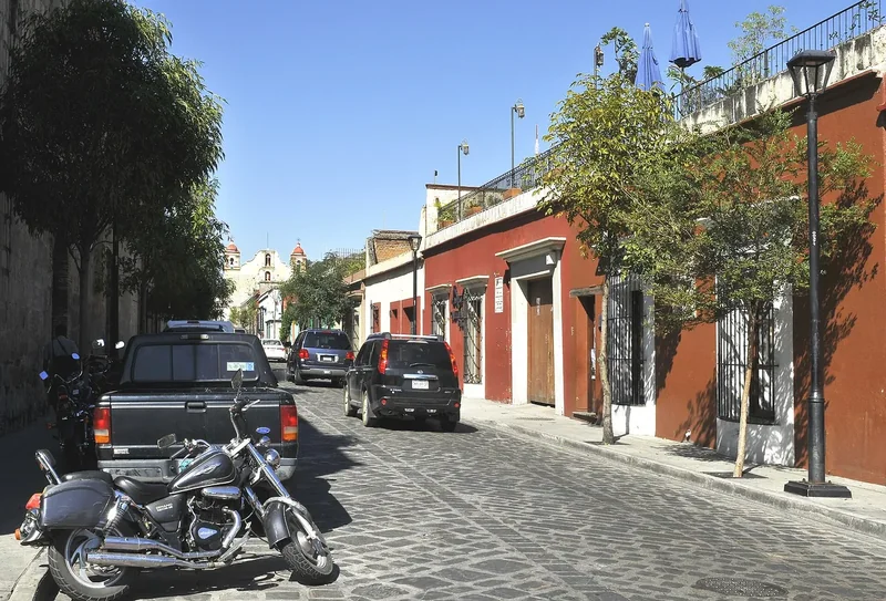 A cobbled street with parked cars and colonial facades in the Centro of Oaxaca