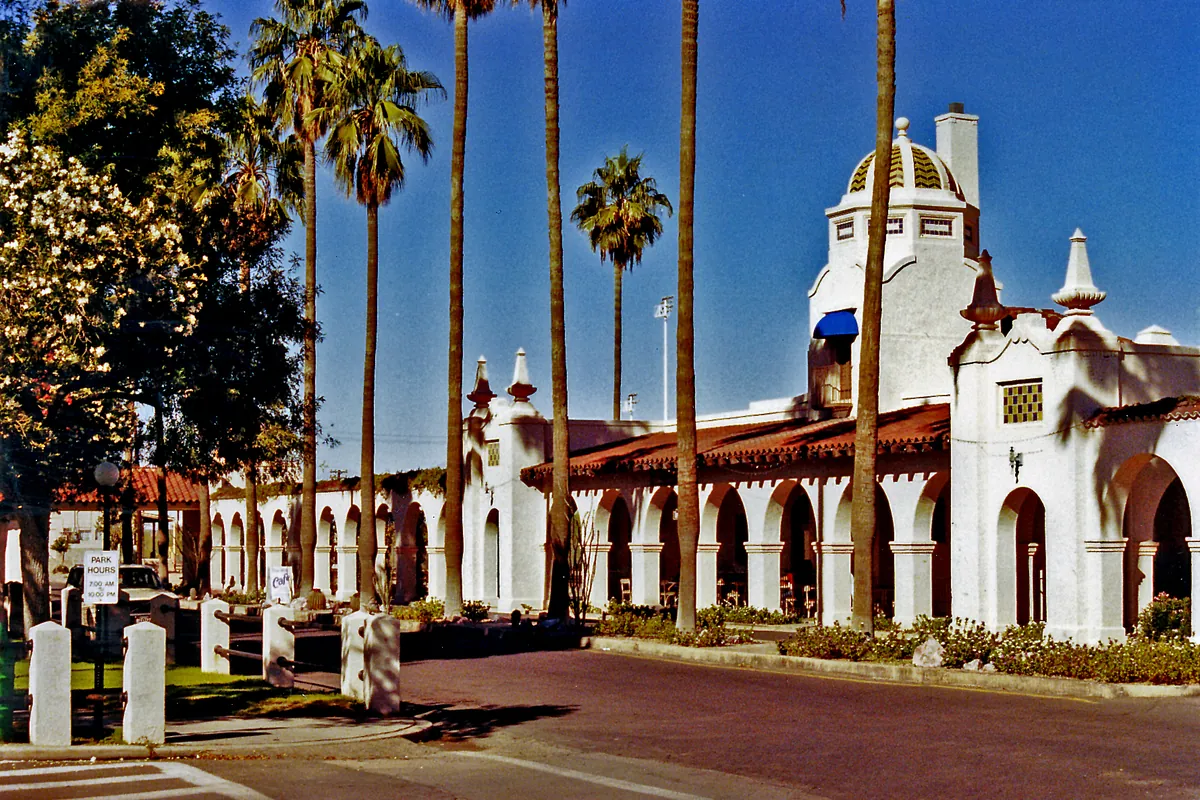 The white Spanish Colonial Revival arcade of the Ajo Plaza behind tall palm trees under a blue sky