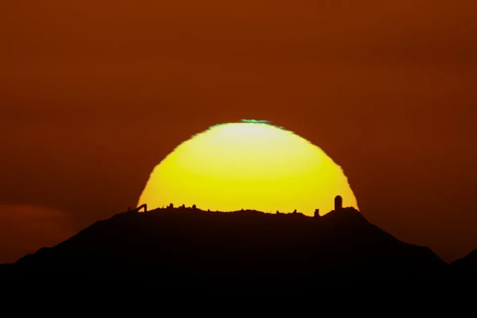The sun setting behind the telescope domes on Kitt Peak, with the desert far below