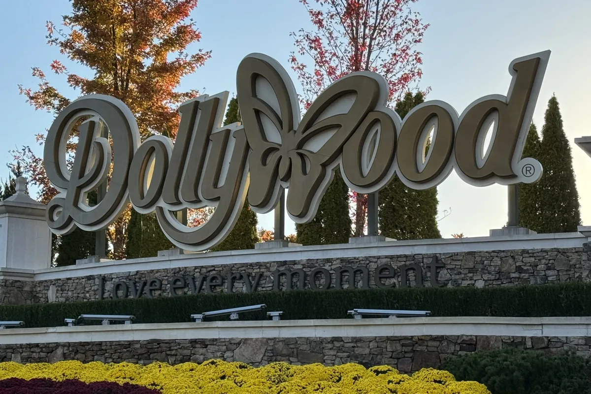 The Dollywood sign above flower beds, with autumn trees behind