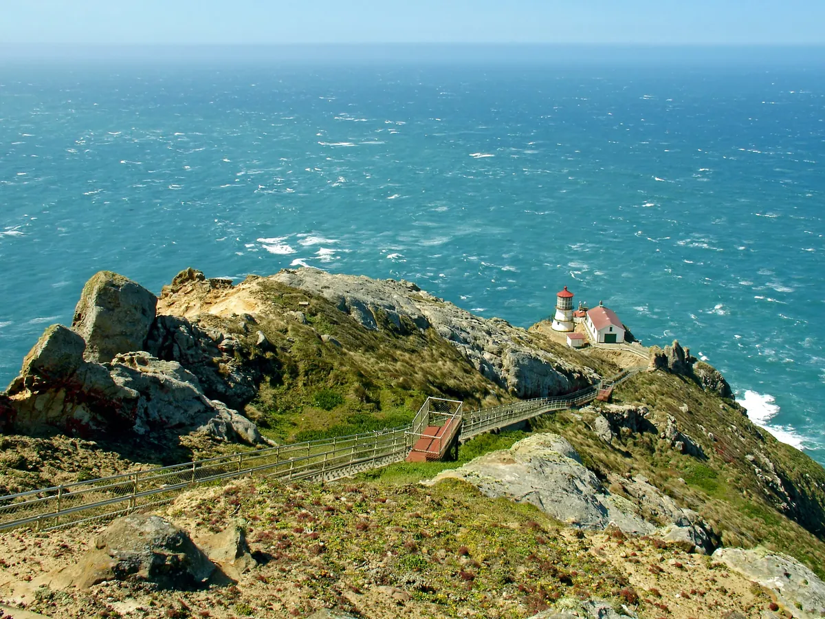 The Point Reyes Lighthouse on a rocky green headland above a deep blue Pacific Ocean