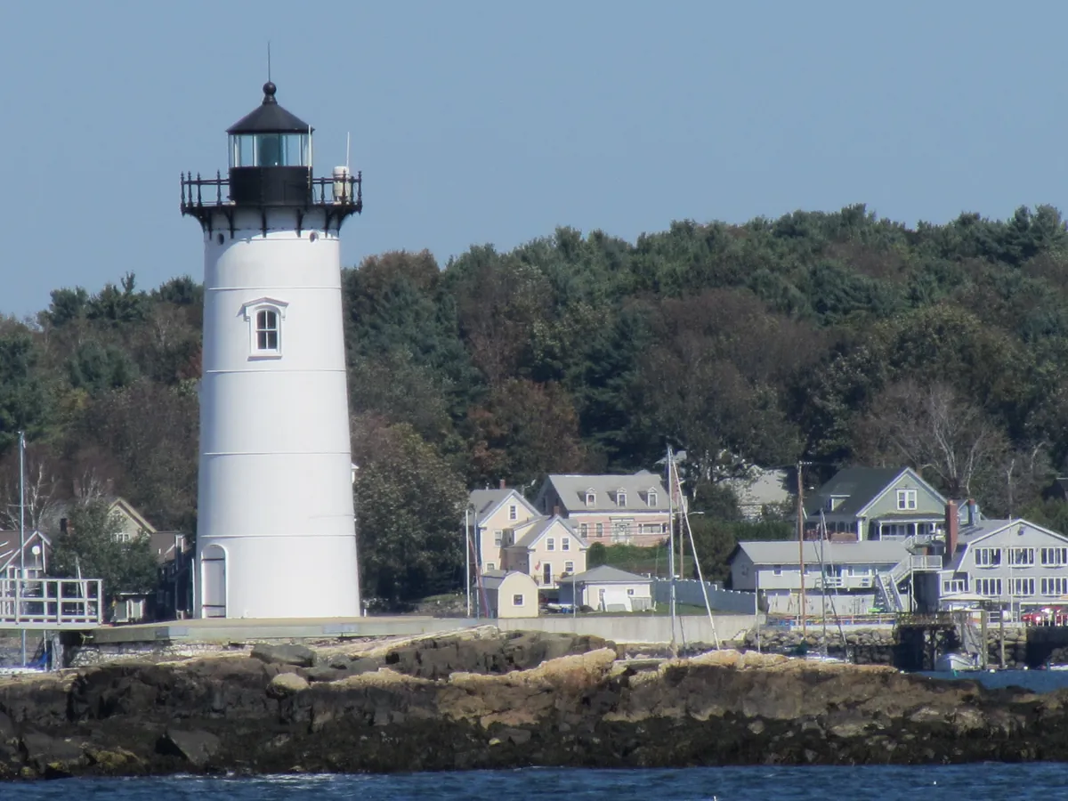 The white Portsmouth Harbor lighthouse on the shore with houses and trees behind