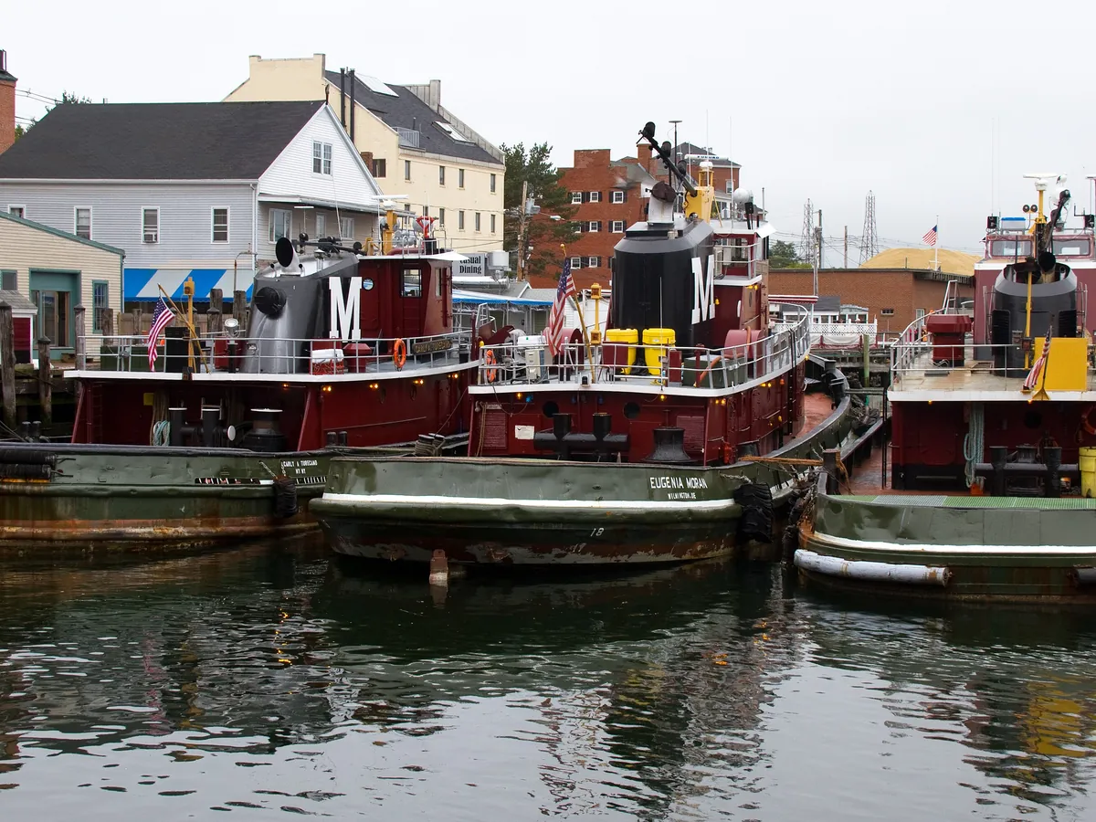 Red-and-black tugboats moored at a wharf in Portsmouth with brick buildings behind