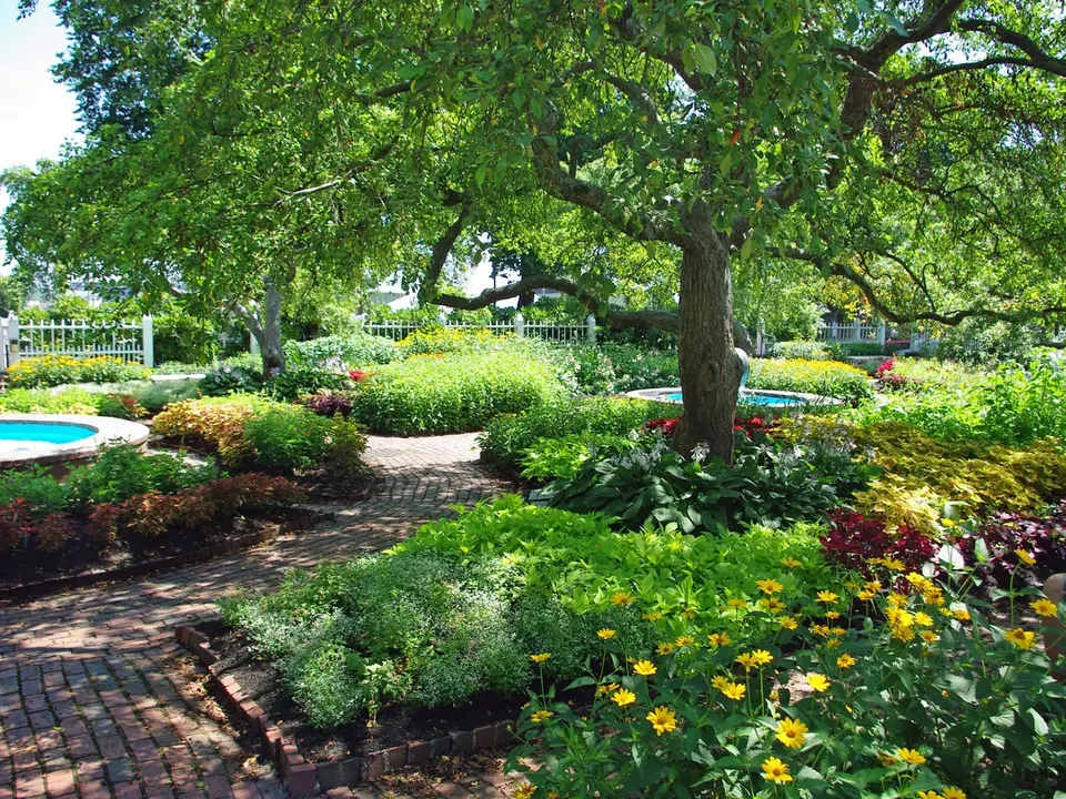Flower beds and brick paths in the gardens of Prescott Park under big shade trees