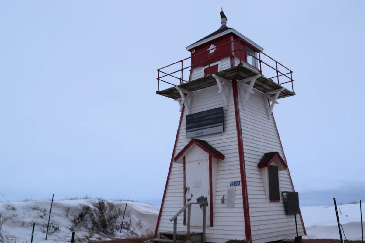 The small white and red wooden Covehead Harbour lighthouse on the dunes