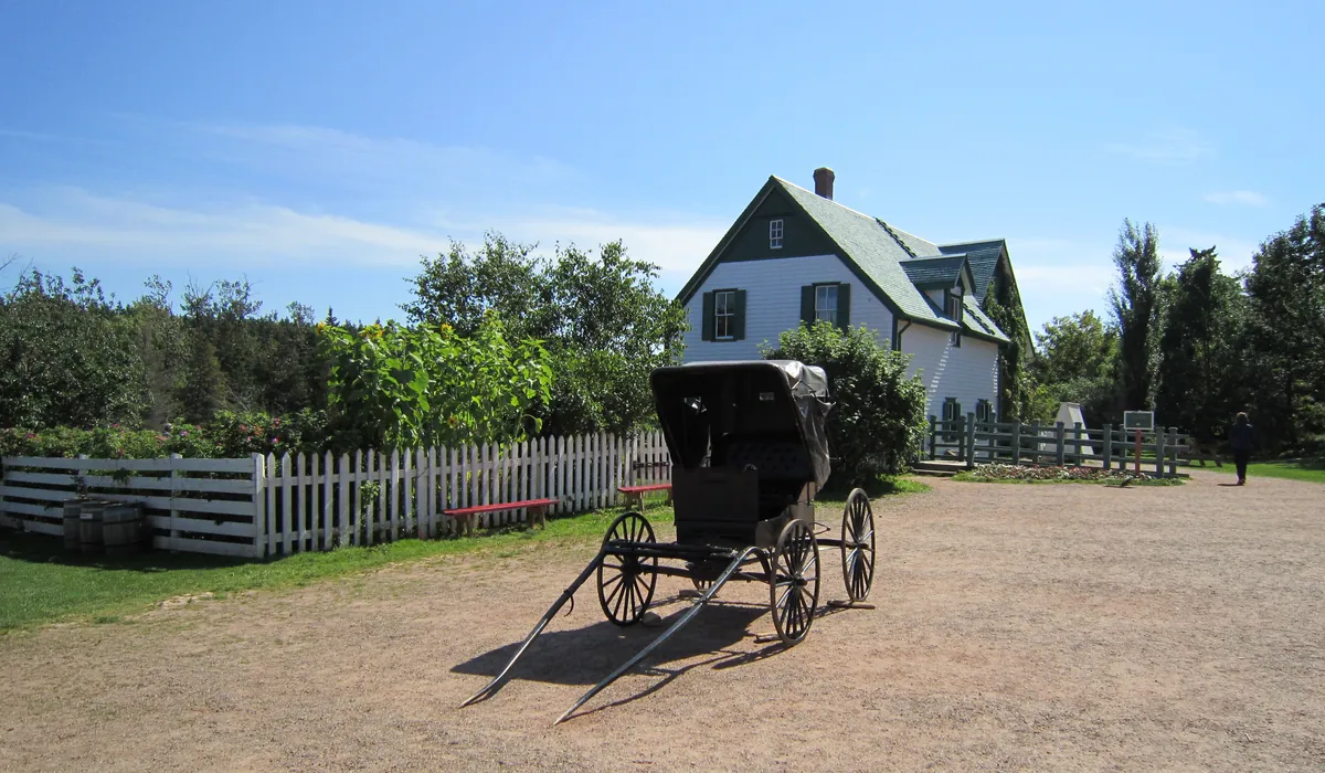 The white farmhouse with green trim at Green Gables Heritage Place, with an old horse buggy on the lane