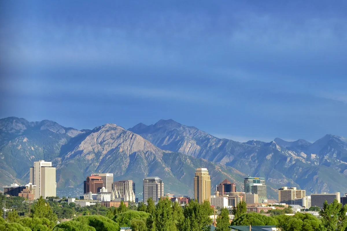 Downtown Salt Lake City towers below the jagged Wasatch Range under a blue sky