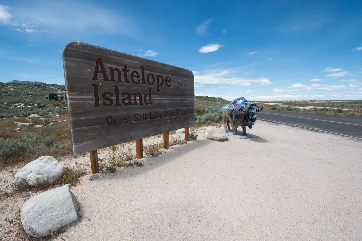The Antelope Island sign beside the road, with a bison statue next to it