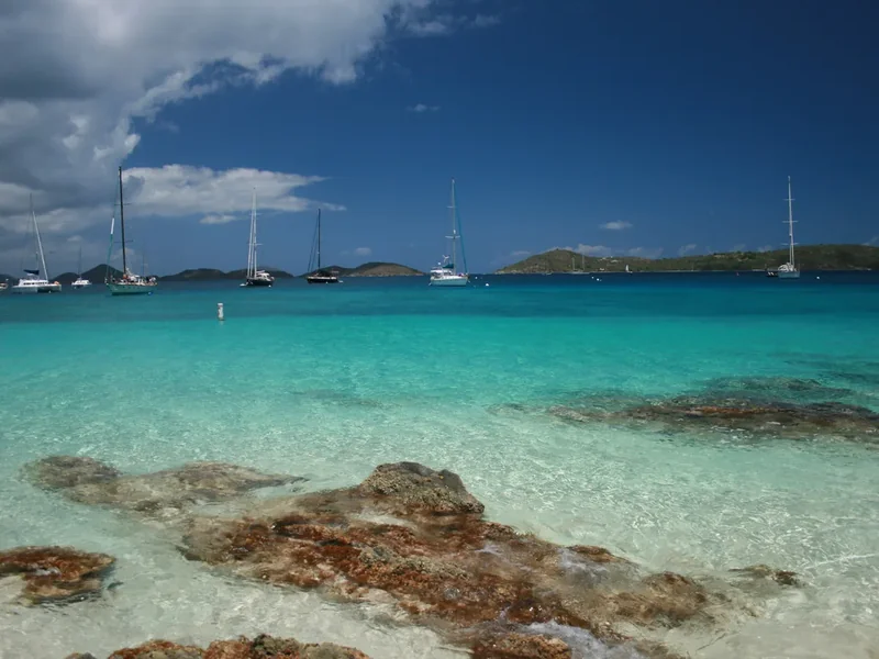Clear shallow water over rocks at Salomon Bay with sailboats moored offshore