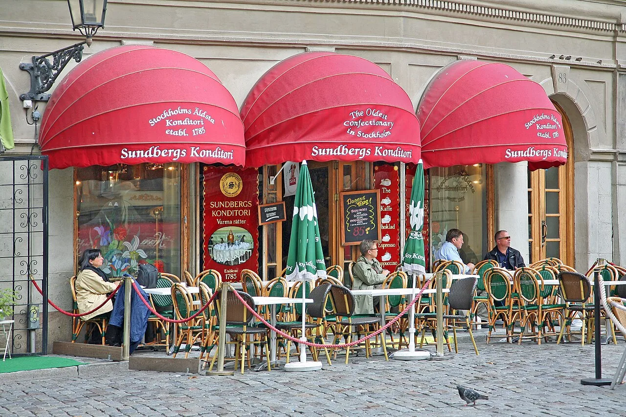 A Gamla Stan café terrace with red awnings, set for fika