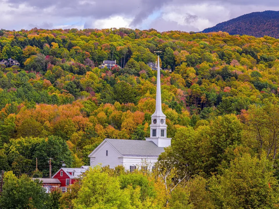 The white Stowe Community Church with its tall steeple among trees on a hillside