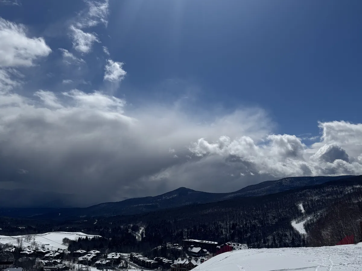 Snowy ski trails at Stowe under a big blue sky with clouds over the mountains
