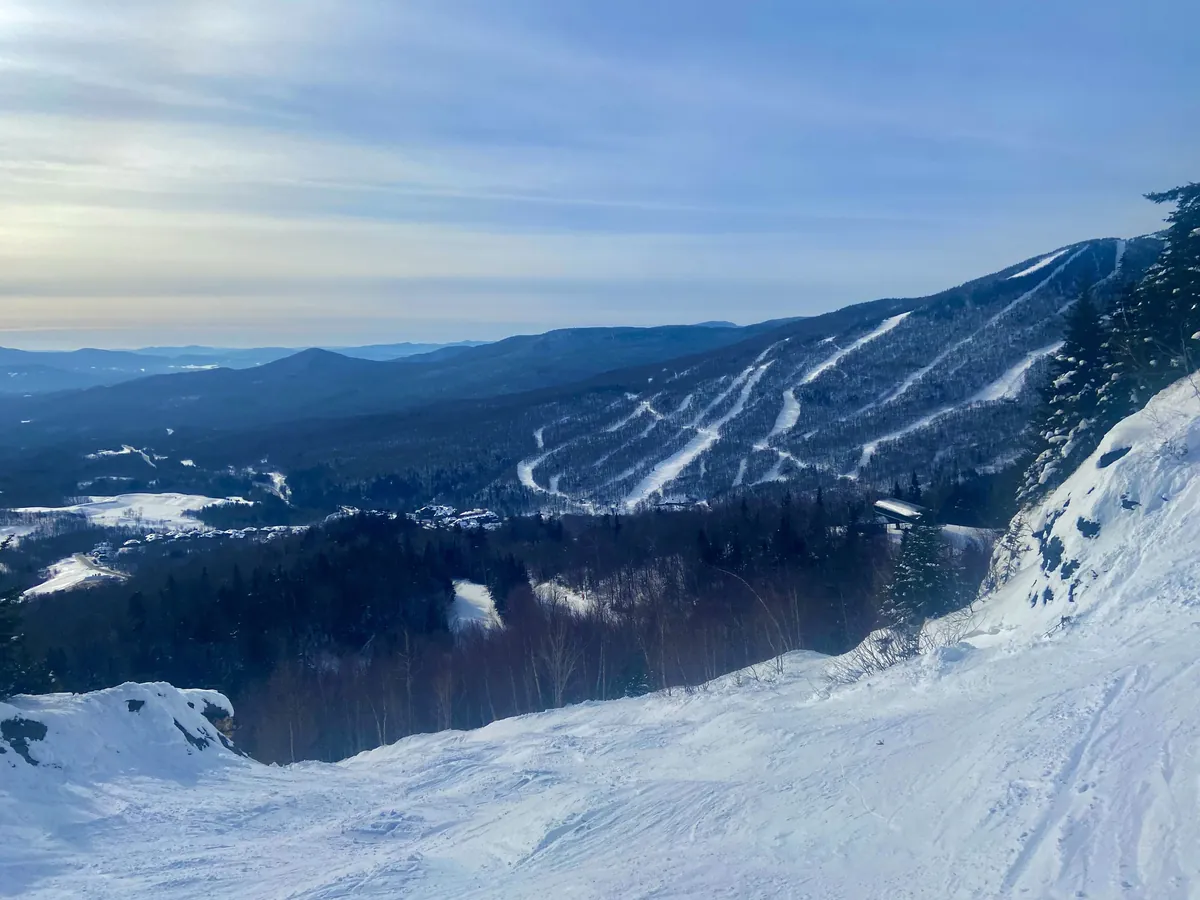 A snowy ski slope at Stowe with mogul runs and ski trails on the forested mountains across the valley