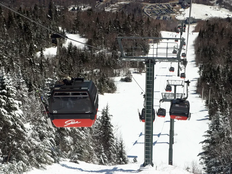Red gondola cabins on a cable above snowy trees at Stowe