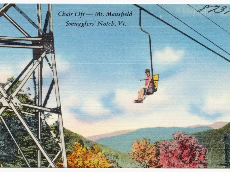An old color postcard of a chairlift at Smugglers’ Notch with a skier riding over autumn trees