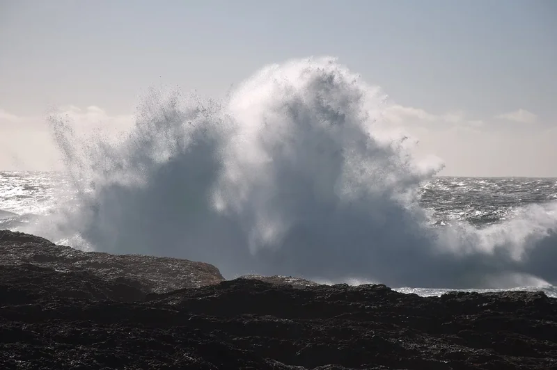 A large wave exploding into spray over dark rocks on Chesterman Beach near Tofino