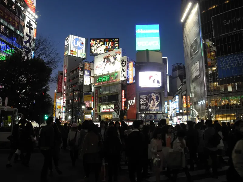 Crowds waiting at Shibuya Crossing at night under bright video screens and lit storefronts