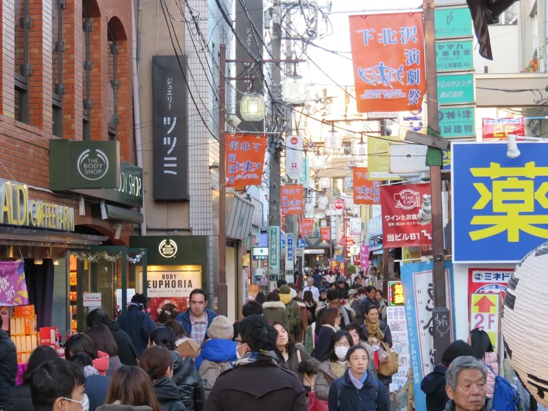 A narrow street in Shimokitazawa crowded with small shops, signs and people walking
