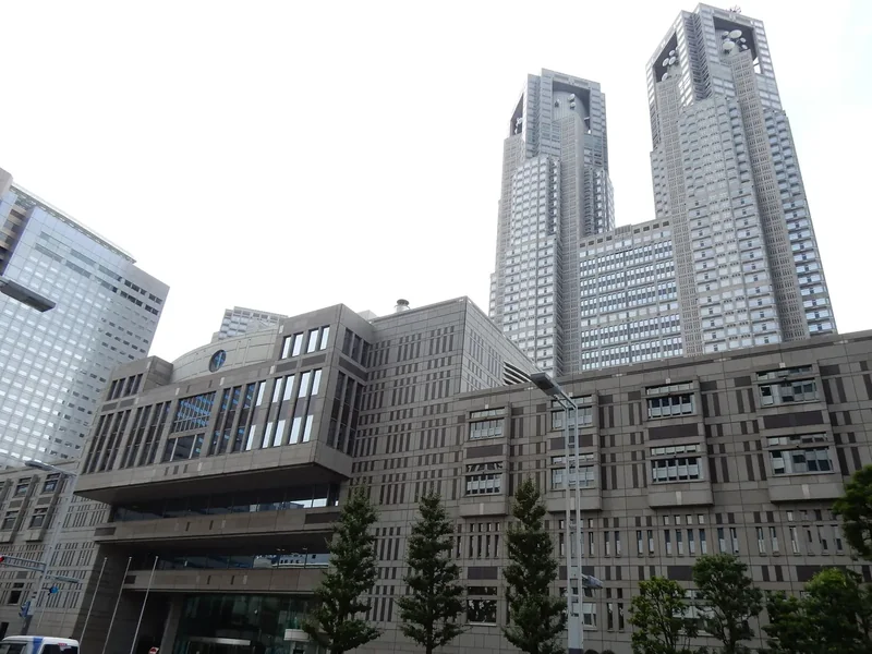 The twin towers of the Tokyo Metropolitan Government Building in Shinjuku against a pale sky