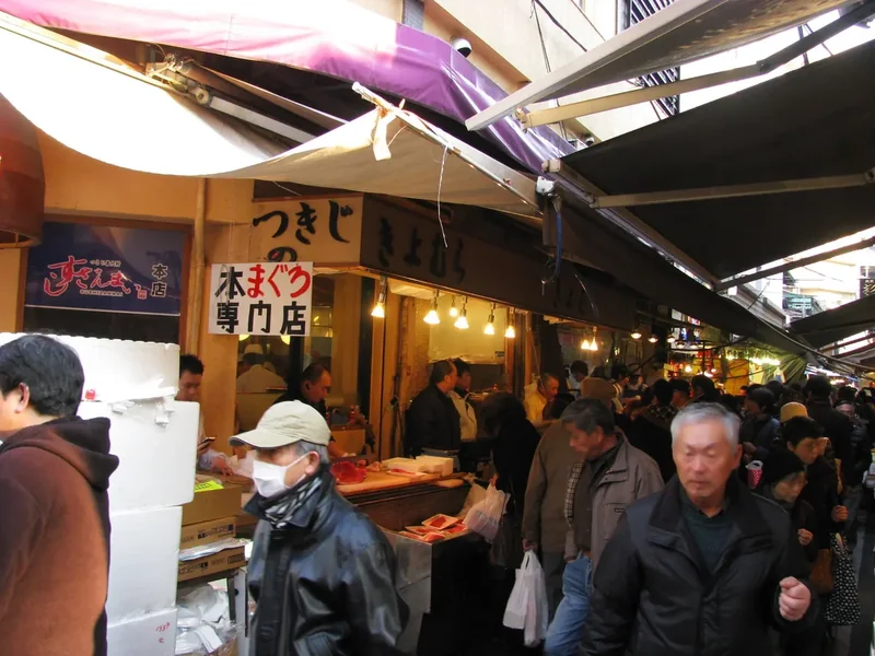 Shoppers in a busy lane of the Tsukiji Outer Market lined with food stalls and signs