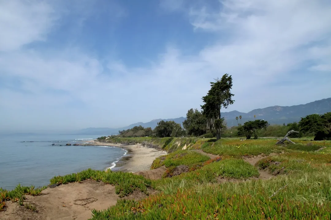 The wide sandy beach at Carpinteria State Beach with low waves and hills behind