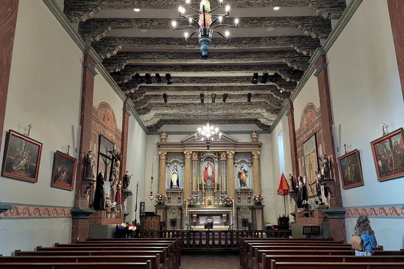 The decorated interior of Mission San Buenaventura, with wooden pews and the altar